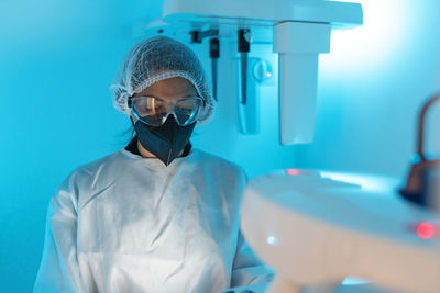 Professional female doctor in medical uniform and protective mask with goggles while using modern diagnostic equipment in hospital