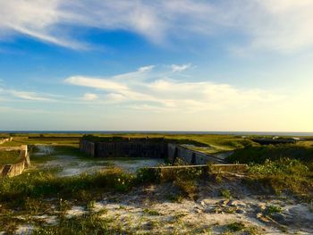 Scenic view of grassy field by sea against cloudy sky