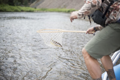 A fly fisherman pulls a brown trout of the river with a net.