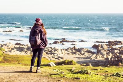 Rear view of woman with backpack standing at beach