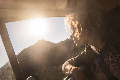 Thoughtful woman looking through window while sitting in camper trailer during sunny day