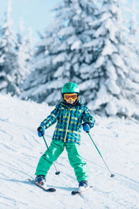 Full length portrait of boy skiing on snow covered land against pine trees