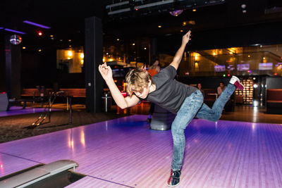 Full length of teenage boy bowling on parquet floor