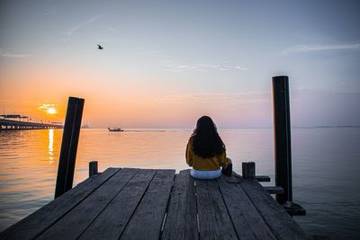 Rear view of woman sitting on pier over sea against sky 