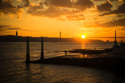 Silhouette bridge over sea against sky during sunset