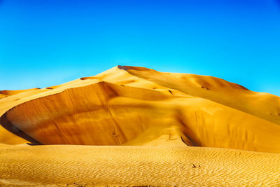 Sand dunes in desert against clear blue sky