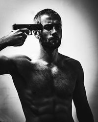 Portrait of shirtless man holding camera over gray background