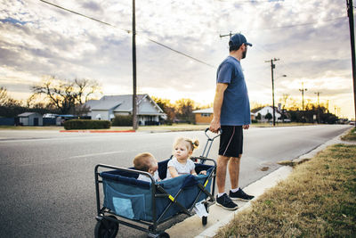 Father holding wagon stroller cart with children sitting in it on road