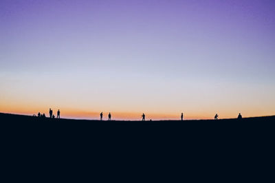 Silhouette people on landscape against clear sky during sunset