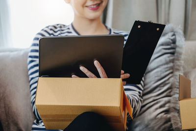 Midsection of woman using digital tablet while sitting on sofa at home