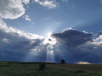 Low angle view of sun streaming through clouds over field