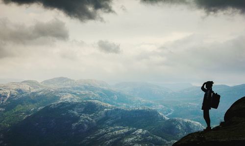 Side view of silhouette woman standing on cliff by mountains