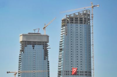 Low angle view of crane by building against clear sky