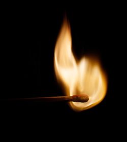 Close-up of burning candle against black background