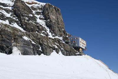 Low angle view of snowcapped mountain and hut against clear blue sky