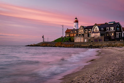 Sea and buildings against sky during sunset