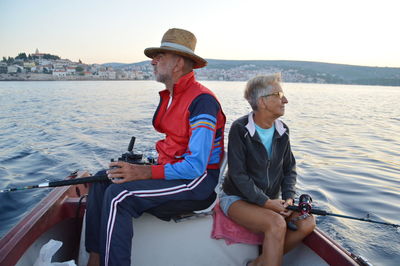 Senior man and woman sitting on boat in river against sky