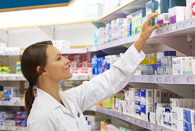 Smiling pharmacist examining medicine on rack in chemist