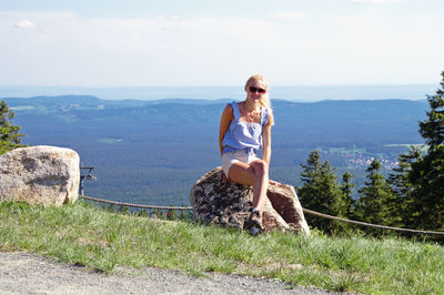 Full length of woman sitting on rock against landscape