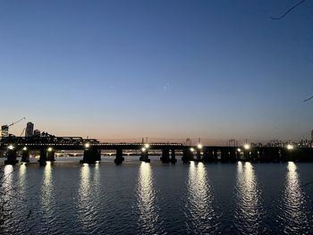 Illuminated bridge over river against sky during sunset