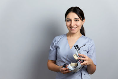 Portrait of young woman standing against gray background