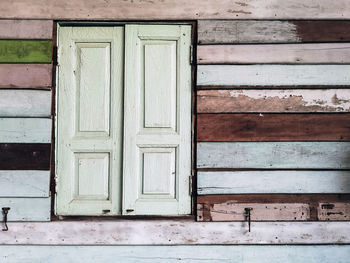 Old grunged wooden window frame painted white vintage with old colourful plywood wall. 