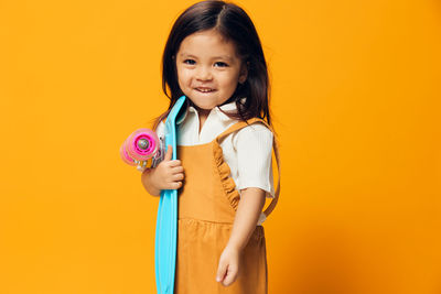 Cute girl with skateboard standing against yellow background