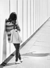 Rear view of woman leaning against wall