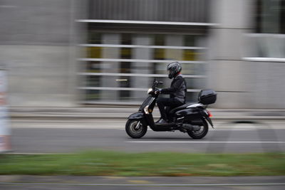 Blurred motion of man riding motor scooter on road