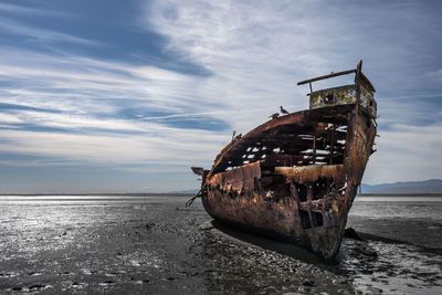 Abandoned boat on sea shore against sky