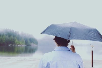 Rear view of man holding umbrella against sky during rainy season