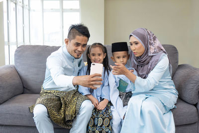 Full length of father and daughter sitting on sofa at home