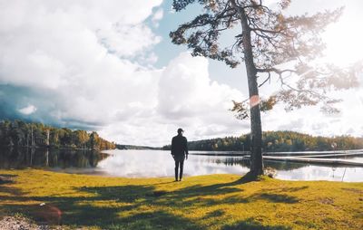 Rear view of man standing by lake against cloudy sky