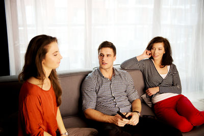 Friends talking while sitting on sofa at home