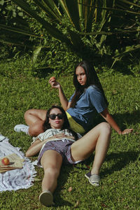 Friends resting on grassy field at park during sunny day