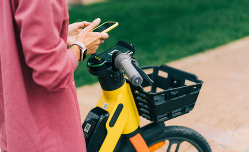Unrecognizable cropped woman rents an electric city bike using an app on her phone.