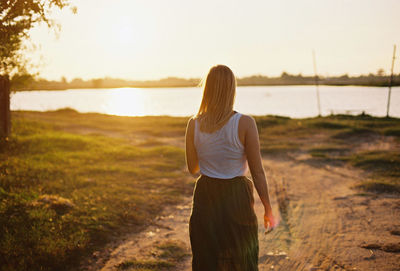 Rear view of woman walking towards lake against sky 