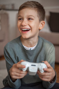 Smiling boy holding video game remote control in living room at home 