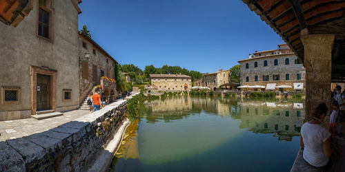 People on canal amidst buildings against sky in city