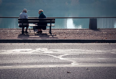 Couple sitting on bench against lake