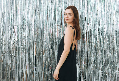 Fashion beauty portrait of young woman with dark long hair in black dress on sparkle background