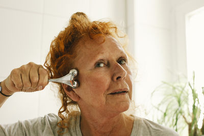 Elderly woman with redhead massaging face at home