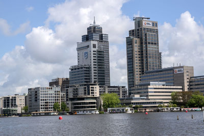 Modern buildings by river against sky in city