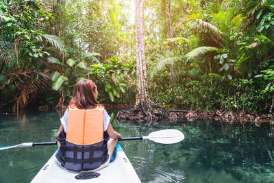 Rear view of man sitting on boat in forest