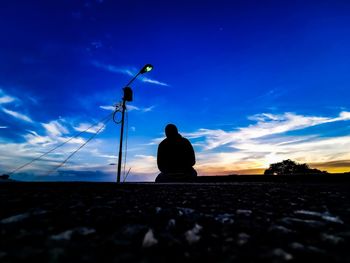 Silhouette person sitting on land against sky during sunset