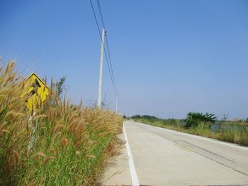 Road amidst field against clear blue sky