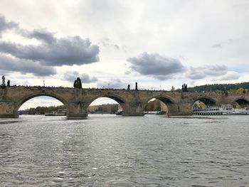 Arch bridge over river against cloudy sky