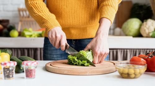 Midsection of woman cutting celery on board in kitchen