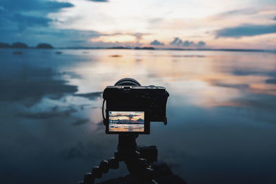 Reflection of camera on sea against sky during sunset