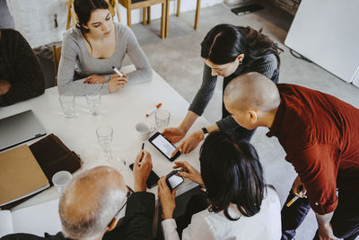 High angle view of female hacker discussing over smart phone with advisors at office